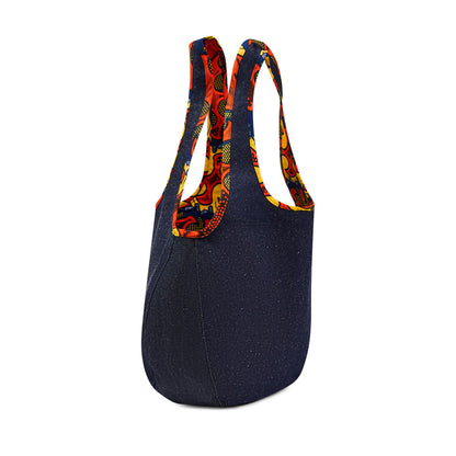 Side profile of the Kalia Denim reversible Hobo bag lined with Zumba African 
printed fabric, and Zumba African printed fabric piping around the handles against a white back ground.