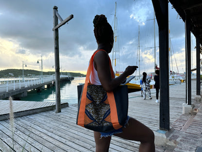 Woman dressed in jeans and a white vest top holding the Mini Kelaya over her right shoulder on the broad walk of wharf with docked boats.