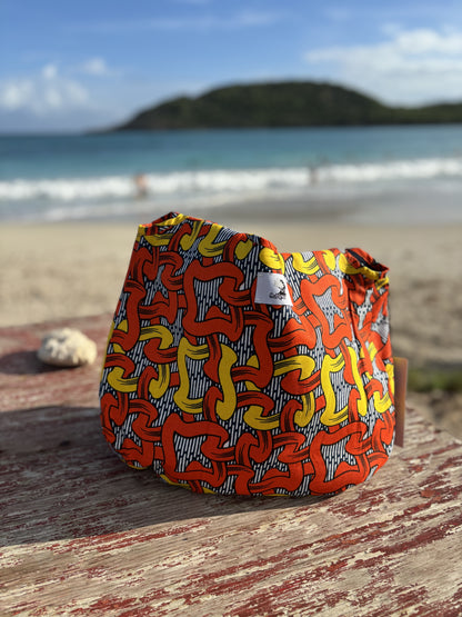 Reversible Denim citrus burst print Kalia Hobo shoulder bag, reserved to show the  citrus burst African printed lining standing on a wooden bench against the back drop of the sea with rolling waves and an island in the far distance.